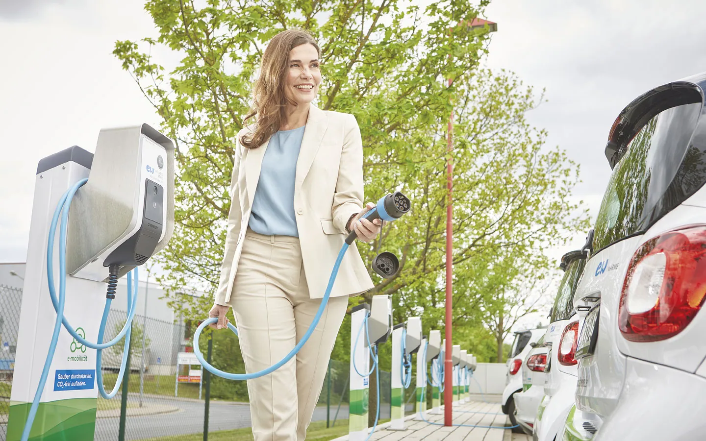 E-Mobilität - Kundin vor Ladestation mit Stecker in der Hand &middot; ARNOLD Elektrotechnik